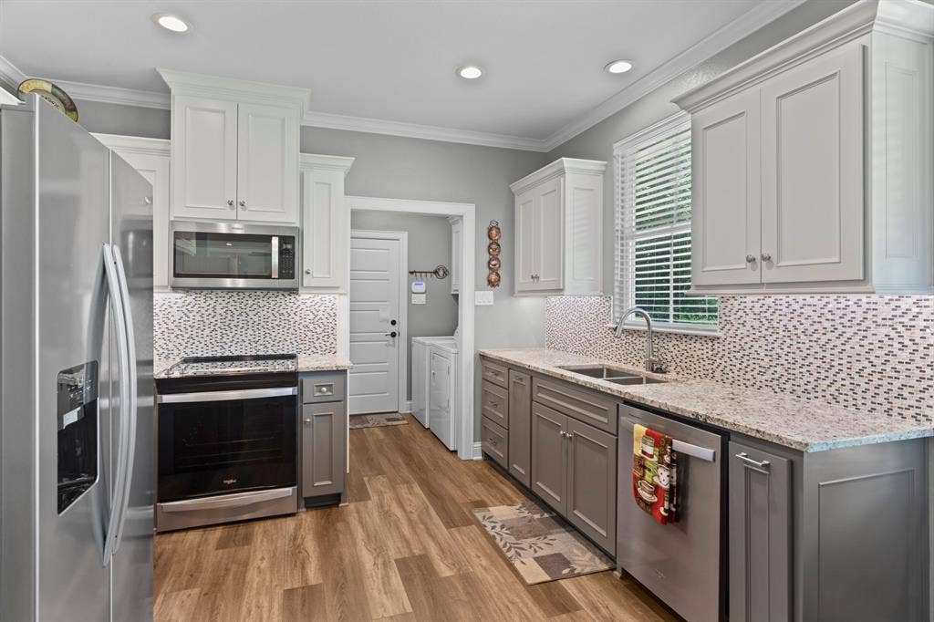 16713 Creek Bottom Court, Winona, TX 75792 Kitchen featuring two-tone cabinetry, stainless steel appliances, granite countertops, and a mosaic tile backsplash