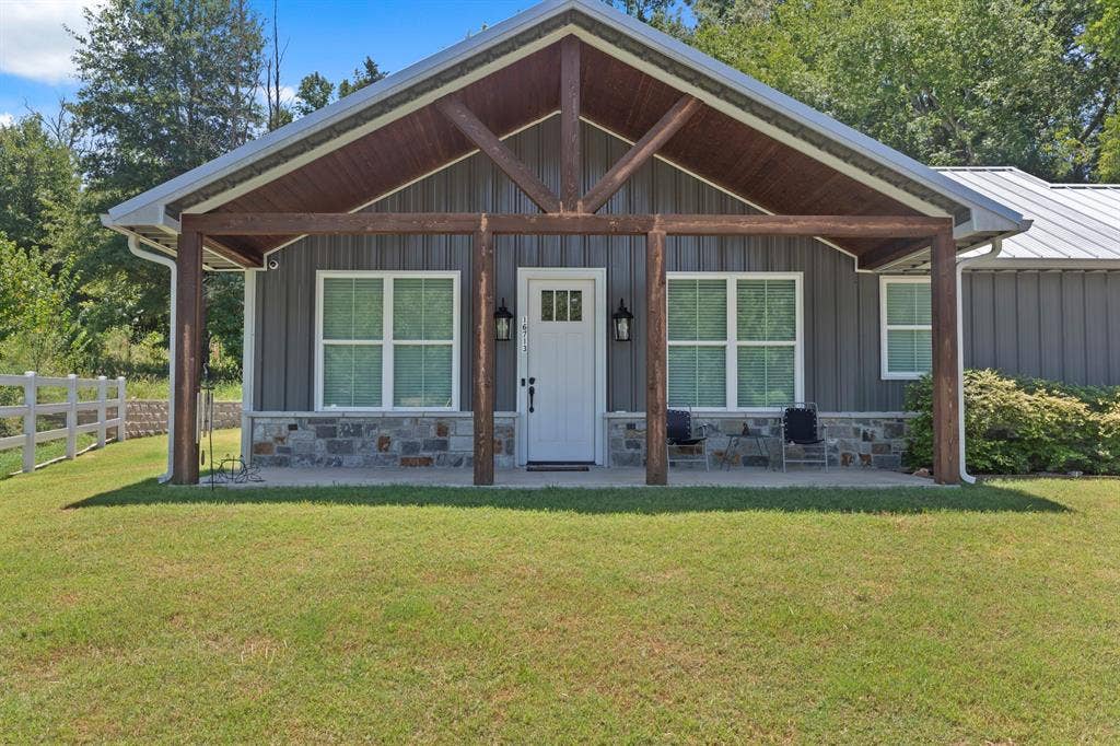 16713 Creek Bottom Court, Winona, TX 75792 Covered porch with exposed wood beams, board and batten siding, stone veneer accents, white paneled entry door, and a metal roof