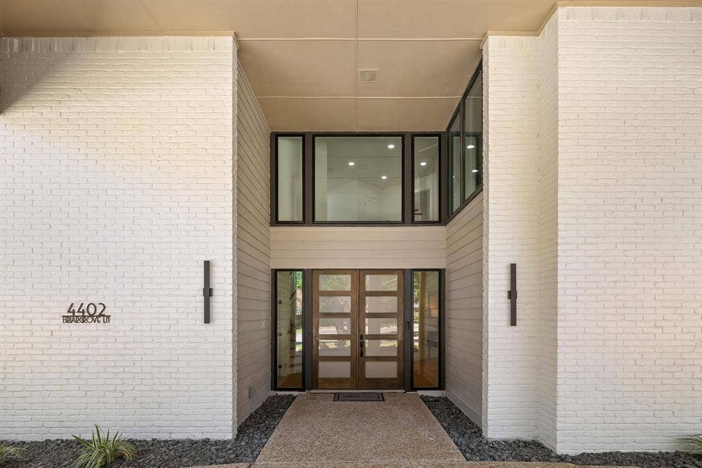 4402 Briargrove Lane, Dallas, TX 75287 4402 Briargrove- White brick exterior with vertical siding accents, prominent transom windows, and a striking double-door entry with dark-framed detailing.