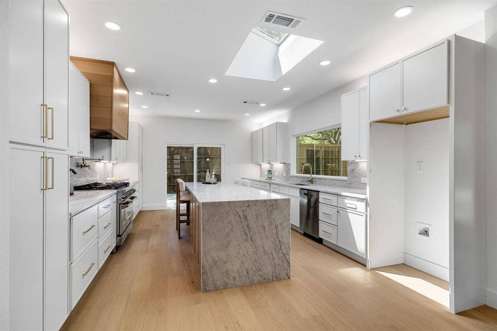 4402 Briargrove Lane, Dallas, TX 75287 4402 Briargrove-Designer kitchen featuring an oversized central island, overhead skylight, wide-plank white oak flooring, shaker white cabinetry, stainless steel appliances