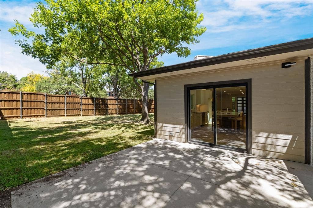 4402 Briargrove Lane, Dallas, TX 75287 4402 Briargrove-Expansive backyard featuring a manicured lawn, wood privacy fence, mature trees, and a concrete patio with sliding glass doors