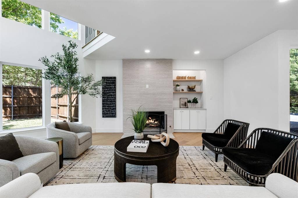 4402 Briargrove Lane, Dallas, TX 75287 4402 Briargrove-Sunlit living space featuring high ceilings, wide-plank white oak flooring, a stone-clad fireplace, and custom built-in shelving and cabinetry.