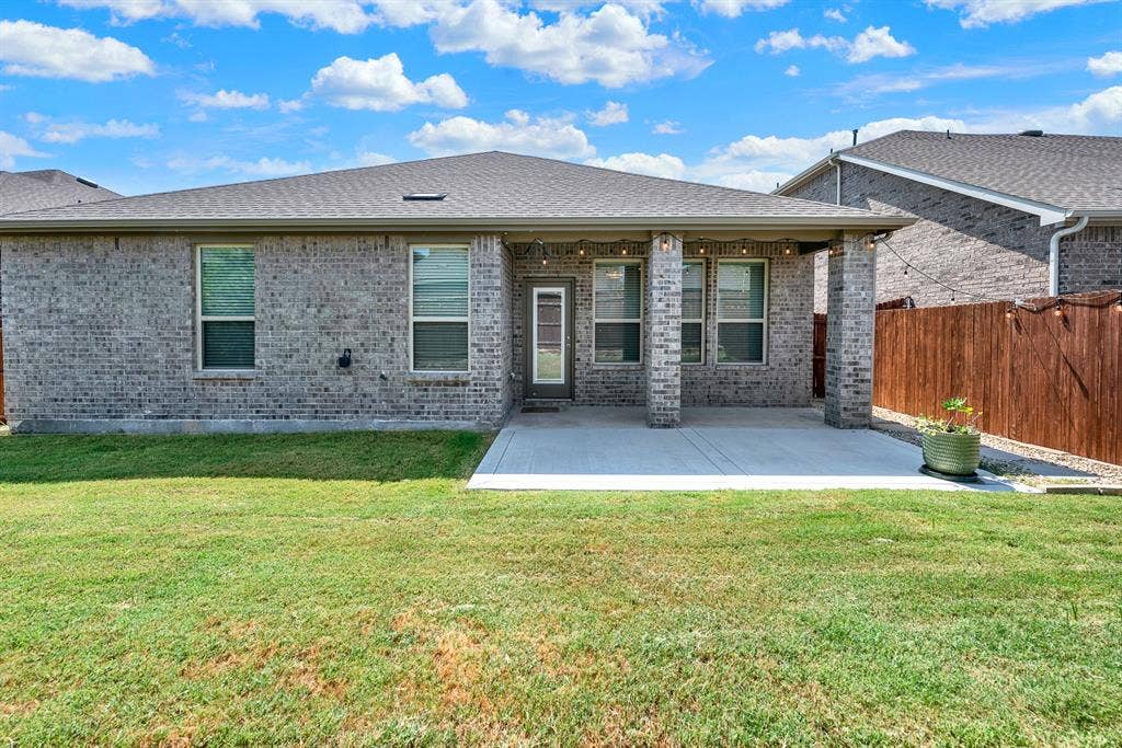 Framed by brick support pillars, this shaded back patio opens directly to a lush, fully fenced lawn backed by a stone-retained wood fence. It offers a cool spot to sip your morning coffee while taking in the open view.