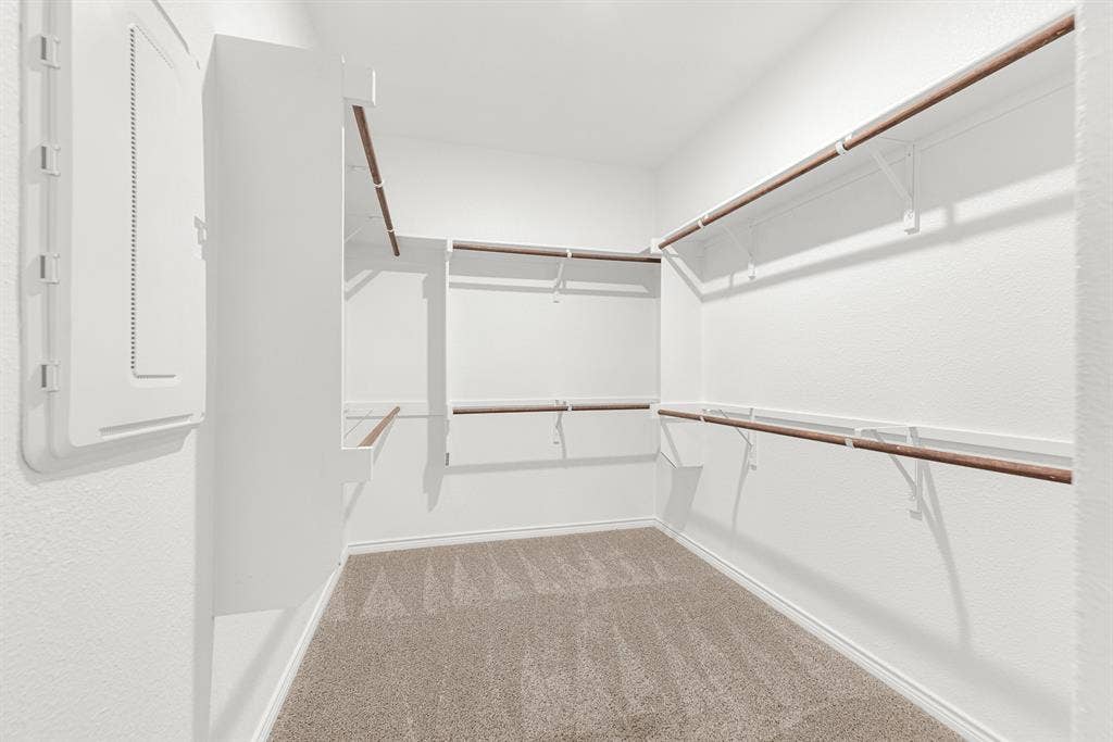 The generous primary closet is fully detailed here, showcasing extensive, multi-level hanging rods and built-in shelving across its carpeted floor. Stay organized effortlessly with this massive storage space that easily accommodates clothing, shoes, and all your storage needs.