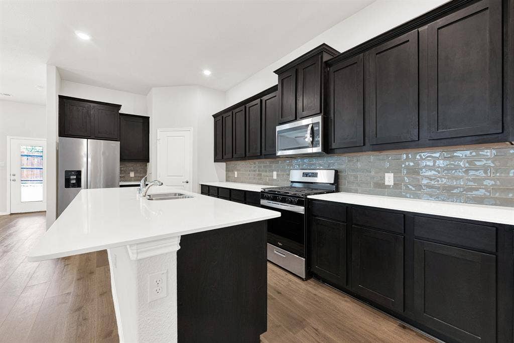 This close-up shot focuses on the main cooking wall, showing the full appliance package with gas range and the contrast between the cabinetry and backsplash. Meal preparation is a joy with modern tools in such a well-appointed, attractive space.