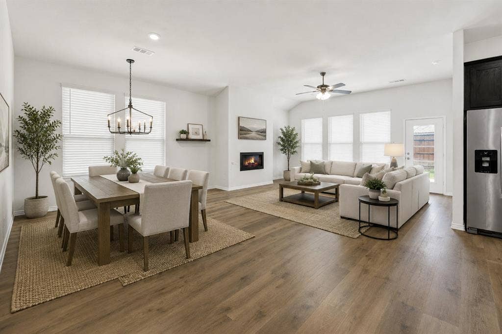A wide angle highlights the spacious open concept layout where extensive LVP wood-look flooring connects the dining area, featuring an inviting fireplace and ample natural light from multiple windows, to the adjacent kitchen. It is the perfect setup for effortless entertaining, allowing conversations to flow easily from dinner prep to relaxing by the fire with friends and family. *Virtually Staged*