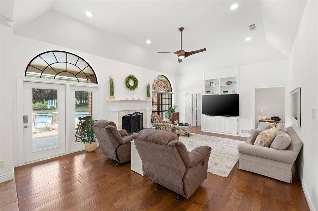 Vaulted ceiling with recessed lighting, wood-finish flooring, white fireplace with a stone surround, built-in cabinetry, and transom windows