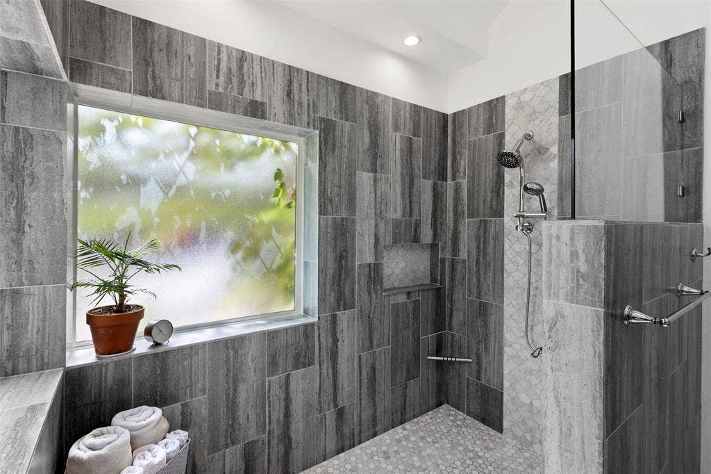 Walk-in shower featuring a built-in bench, glass enclosure, tiled walls, a shower niche, and pebble flooring