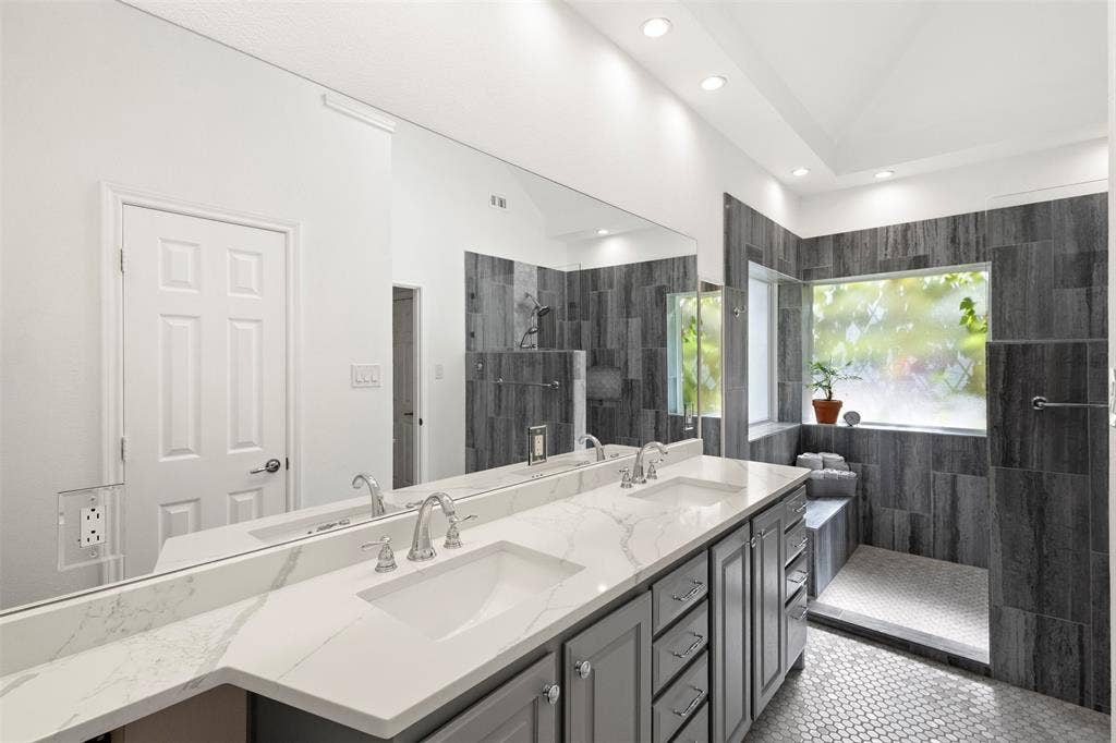 Spa-inspired primary bathroom featuring dual vanities with white quartz countertops, polished chrome fixtures, and abundant mirror lighting