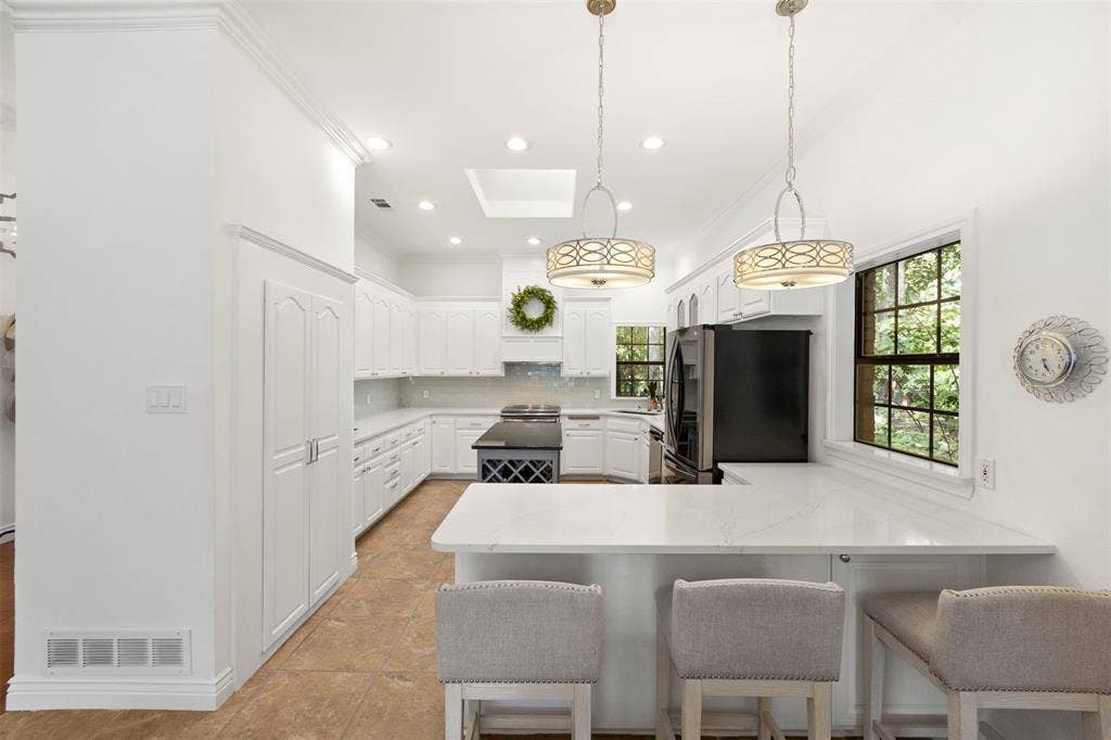 White cabinetry, white countertops, built-in pantry, central island with wine storage, and pendant lighting