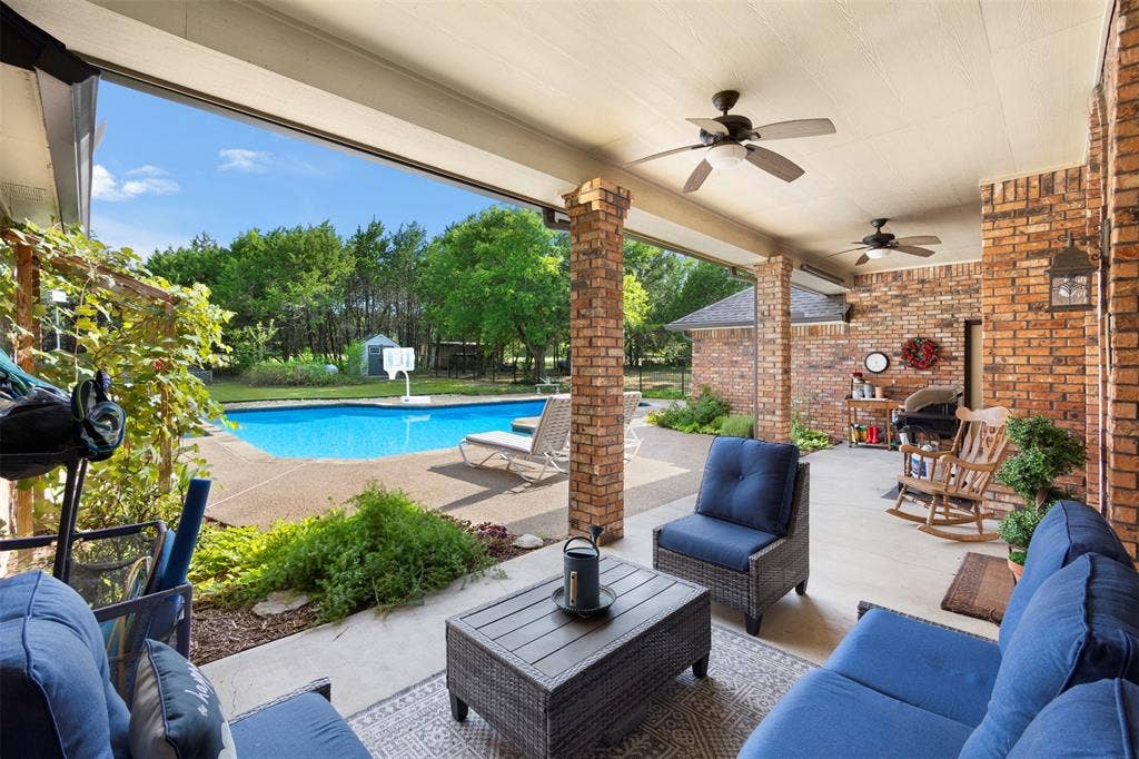 Expansive covered patio with brick columns, dual ceiling fans, and an attached outdoor lighting fixture