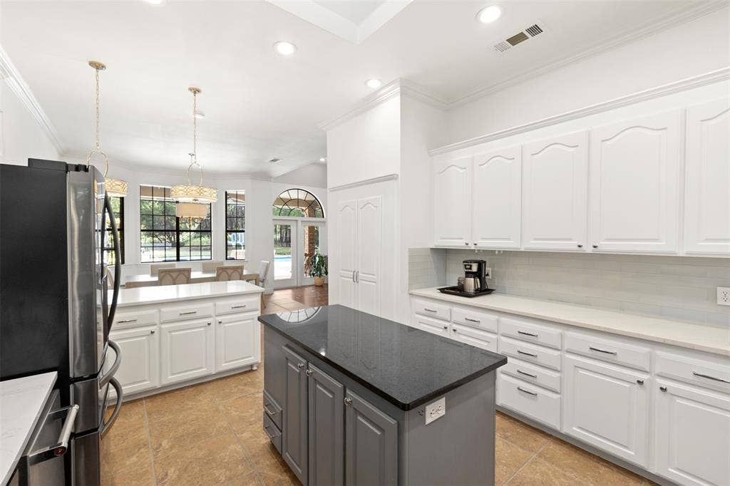 Spacious kitchen featuring white cabinetry, a large gray island with a dark countertop, stainless steel appliances, and tile flooring