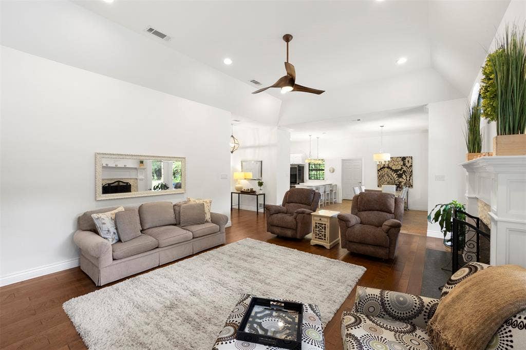 Vaulted ceilings with recessed lighting, hardwood flooring, and a fireplace with a stone surround and mantel