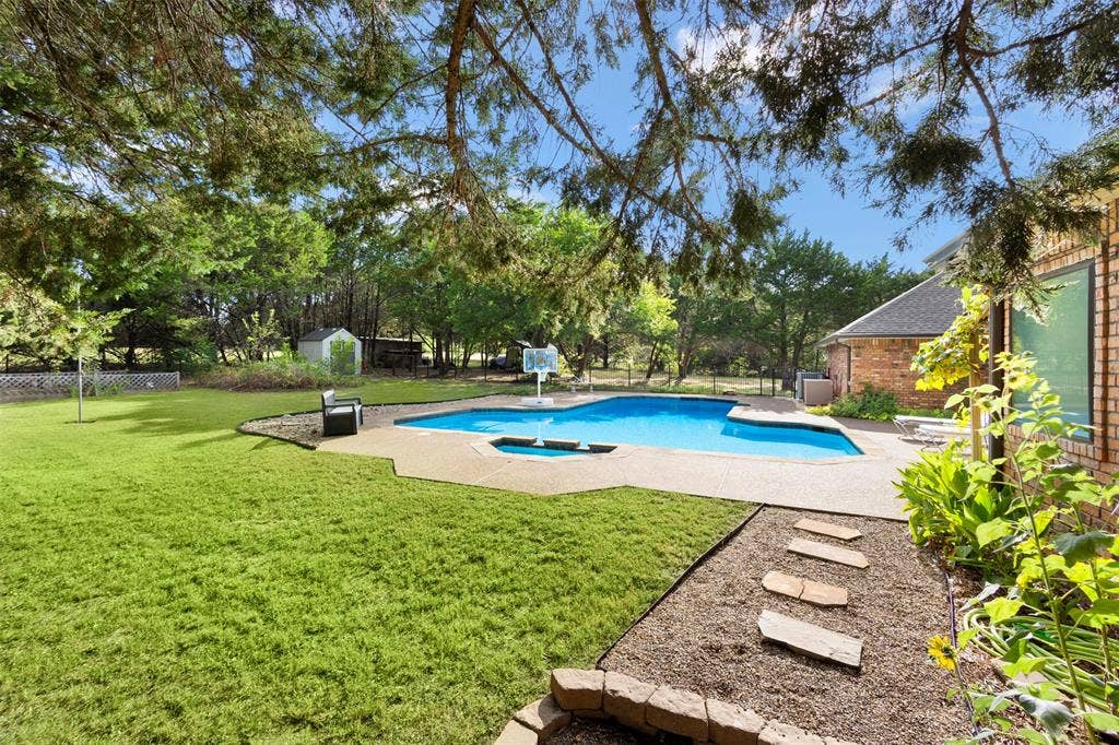 Expansive backyard featuring a swimming pool with integrated spa, concrete decking, stone stepping path, and a storage shed