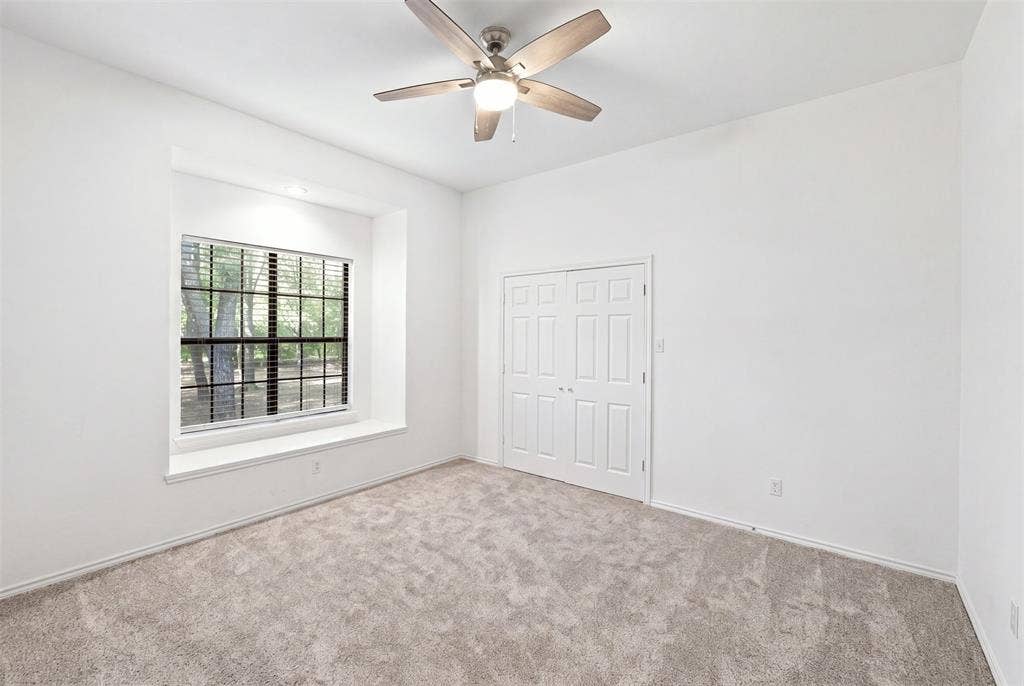 Recessed window with a deep sill, neutral carpeting, crisp white walls, ceiling fan, and double-door closet