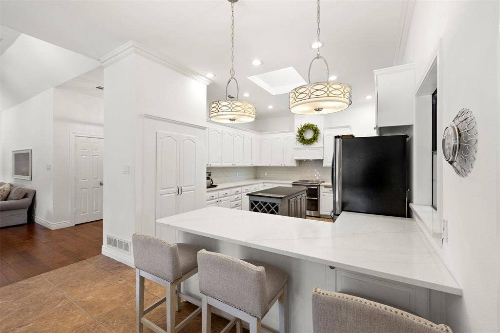 Modern kitchen featuring an eat-at island with a white countertop, white cabinetry, a central island with integrated wine storage, and two decorative pendant lights