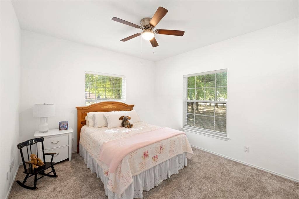 Carpeted flooring, two windows with blinds, ceiling fan with light fixture, and white walls