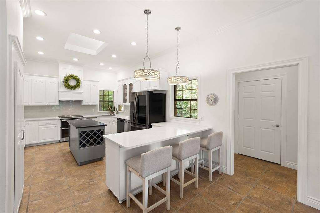 Spacious kitchen featuring white cabinetry, light-toned countertops, a central island with wine storage, and an integrated breakfast bar