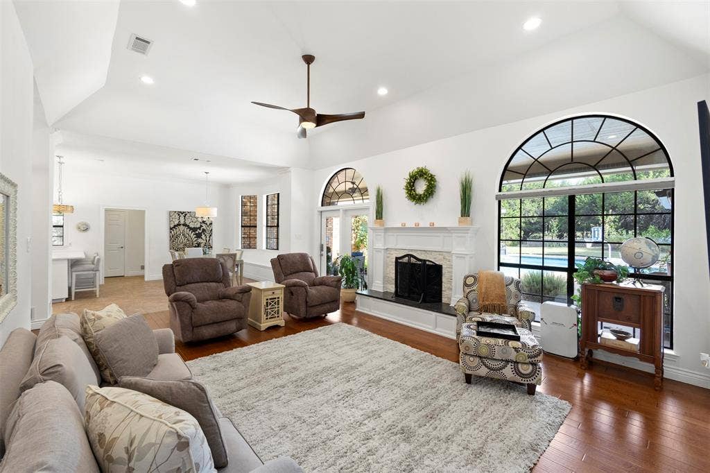 Vaulted ceiling with recessed lighting, wood-finish flooring, white fireplace with dark hearth, and a large arched window with grid details