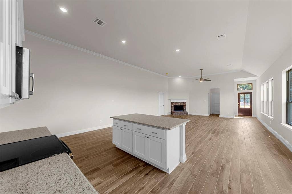 111 WATERCREST Lane, Glenn Heights, TX 75154 Open-concept living space with vaulted ceilings, recessed lighting, wood-finish flooring, stone fireplace, and a kitchen island with stone countertops
