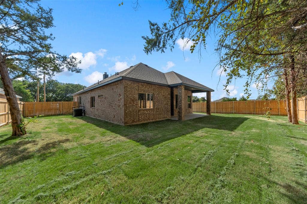 111 WATERCREST Lane, Glenn Heights, TX 75154 Expansive backyard with a manicured lawn, brick exterior, covered patio, and wood privacy fencing