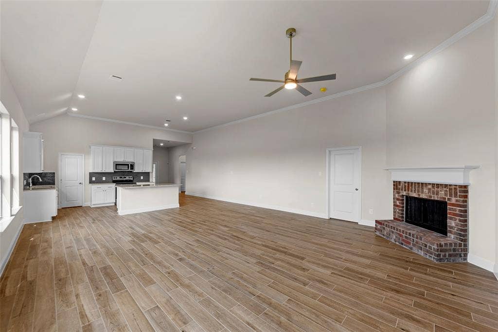 111 WATERCREST Lane, Glenn Heights, TX 75154 Spacious open-concept interior featuring vaulted ceilings, wood-finish flooring, a brick fireplace, and a kitchen with white cabinetry and stainless steel appliances