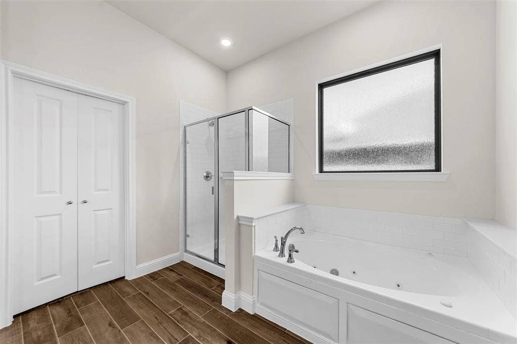 111 WATERCREST Lane, Glenn Heights, TX 75154 Jetted soaking tub with a tiled surround, glass-enclosed shower, wood-finish flooring, and a privacy window