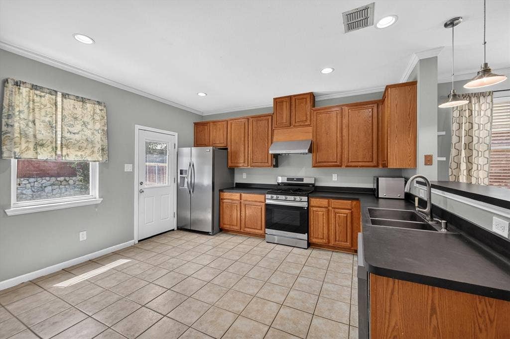 6513 Cartier Court, McKinney, TX 75072 Kitchen featuring wood cabinetry, stainless steel appliances, dark countertops, a double basin sink with a gooseneck faucet, and tile flooring