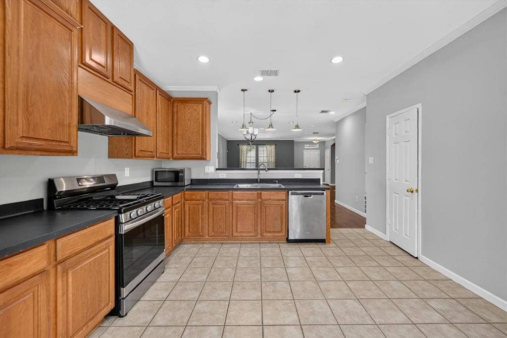 6513 Cartier Court, McKinney, TX 75072 Kitchen featuring wood cabinetry, stainless steel appliances, dark countertops, and tile flooring