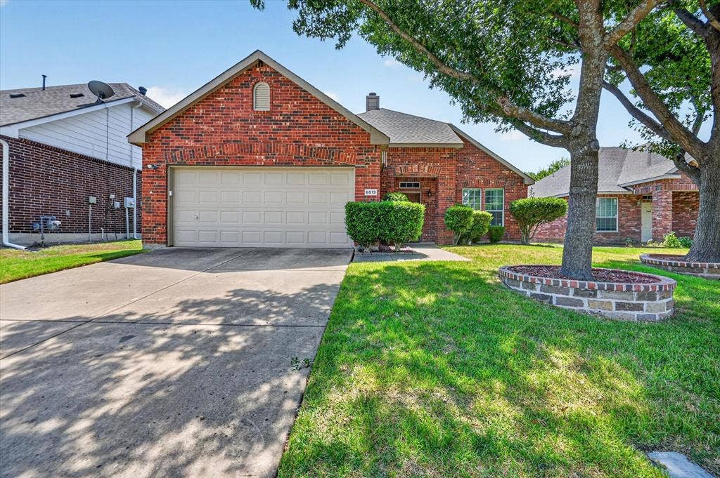 6513 Cartier Court, McKinney, TX 75072 Charming brick home featuring a two-car garage, manicured front lawn with mature landscaping, brick front planter bed, and tree-lined lot with established shade trees