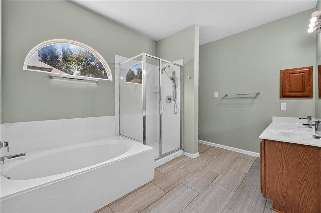 6513 Cartier Court, McKinney, TX 75072 Alcove bathtub with an arched window, glass-enclosed shower, dual vanity with undermount sinks, and tile flooring