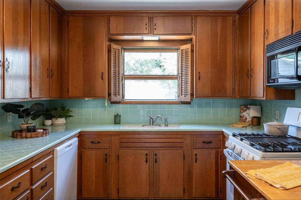 3807 Huaco Lane, Waco, TX 76710 U-shaped kitchen with wood cabinetry, light blue tiled countertops, matching tiled backsplash, and a built-in microwave