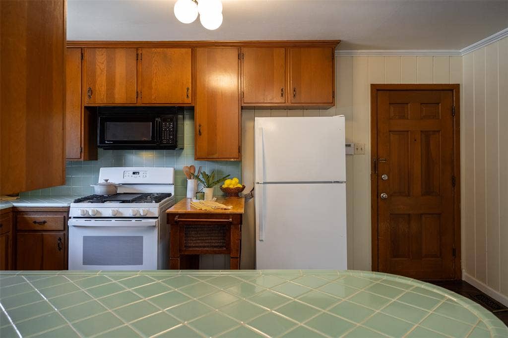 3807 Huaco Lane, Waco, TX 76710 Wood cabinetry, white range, built-in microwave, paneled door, and tiled countertop