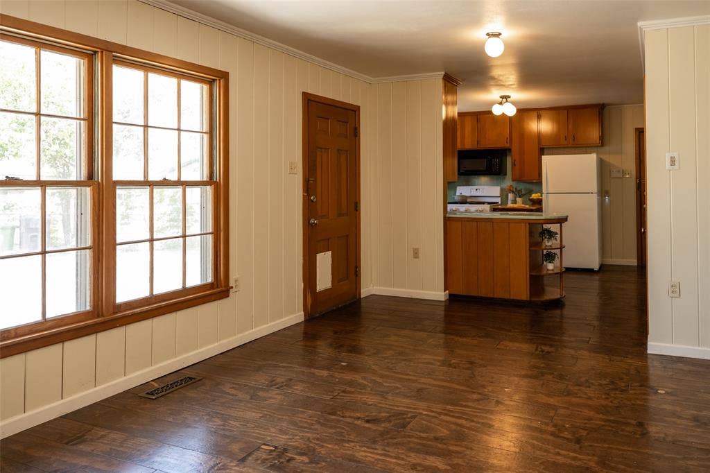 3807 Huaco Lane, Waco, TX 76710 Hardwood-finish flooring, paneled wall detailing, natural wood-frame windows, and a wood-finish entry door with a built-in kitchen featuring wood cabinetry and white appliances