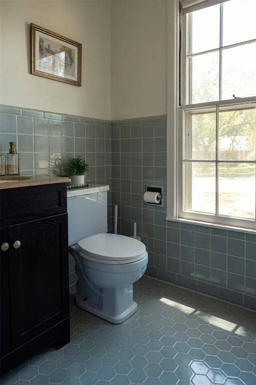 3807 Huaco Lane, Waco, TX 76710 Bathroom featuring a built-in dark wood-finish vanity with a light-toned countertop, a window with multiple panes, light blue hexagonal floor tiles, and light blue square wall tiles
