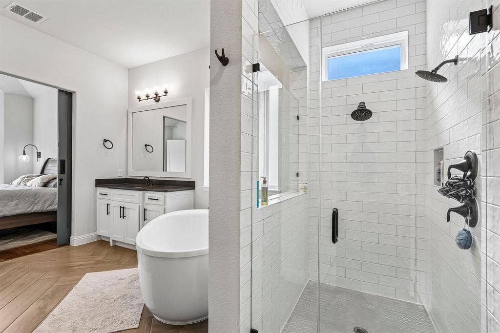 1657 Lilac Lane, Celina, TX 75009 Spacious bathroom featuring a freestanding soaking tub, dual-head shower with subway tile surround, white vanity with dark countertop, and wood-finish flooring