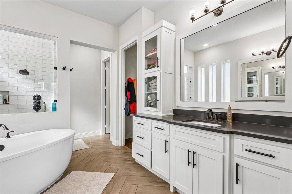 1657 Lilac Lane, Celina, TX 75009 Freestanding soaking tub, walk-in shower with subway tile, dual vanity with undermount sink, dark countertop, and herringbone wood-finish flooring
