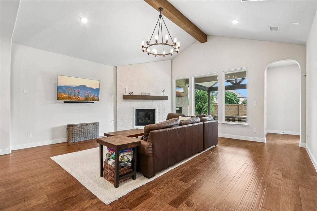 1657 Lilac Lane, Celina, TX 75009 Vaulted ceiling with exposed wood beam, wood-finish flooring, white brick fireplace, arched doorway, and large windows
