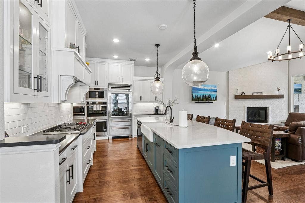 1657 Lilac Lane, Celina, TX 75009 Gourmet kitchen featuring a white subway tile backsplash, stainless steel appliances, a large center island with a farm sink, and wood-finish flooring