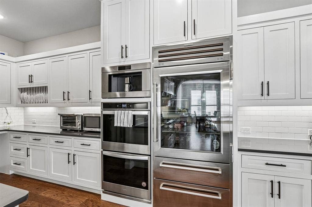1657 Lilac Lane, Celina, TX 75009 White shaker-style cabinetry with matte black hardware, integrated stainless steel appliances, dark countertops, white subway tile backsplash, and wood-finish flooring