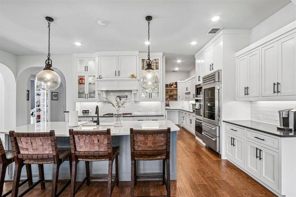 1657 Lilac Lane, Celina, TX 75009 Spacious kitchen featuring white cabinetry, stainless steel appliances, a large center island, wood-finish flooring, and subway tile backsplash