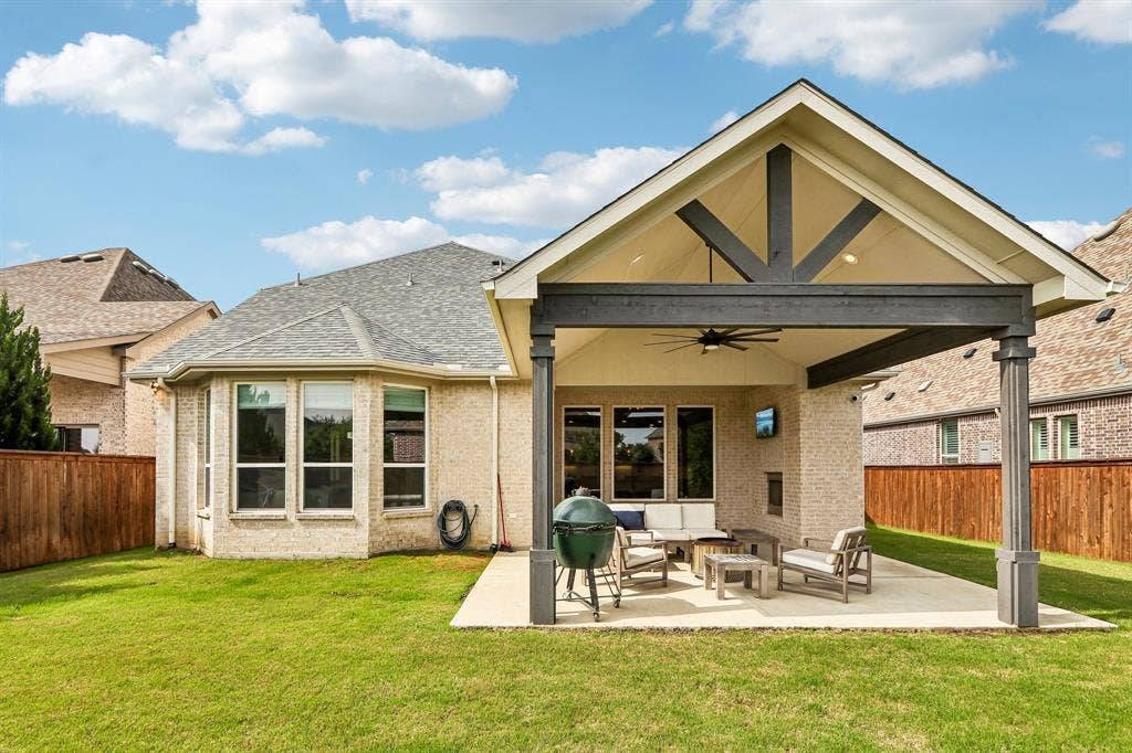 1657 Lilac Lane, Celina, TX 75009 Expansive backyard featuring a covered patio, vaulted ceiling with exposed beams, ceiling fan, and brick fireplace