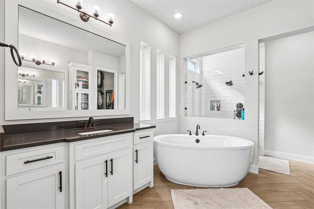 1657 Lilac Lane, Celina, TX 75009 White shaker-style vanity with dark countertop, large framed mirror, freestanding soaking tub, and a glass-enclosed shower with subway tile