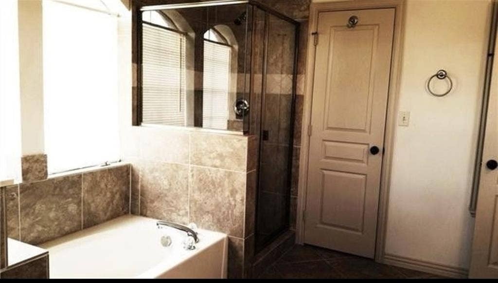 3713 Pearl Trail, Garland, TX 75044 Soaking tub with tile surround, glass-enclosed shower, and arched window with blinds