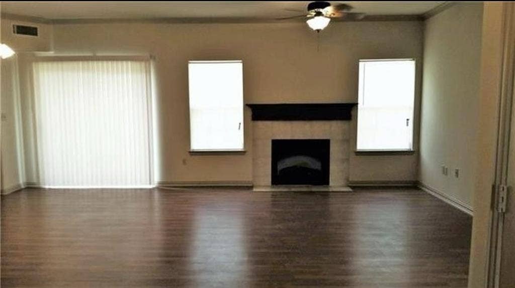 3713 Pearl Trail, Garland, TX 75044 Spacious room featuring wood-finish flooring, a fireplace with a stone surround and dark mantel, a ceiling fan with integrated lighting, and multiple windows with vertical blinds