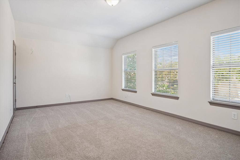 Spacious room featuring multiple windows with blinds, neutral-toned carpet flooring, and a flush mount ceiling light