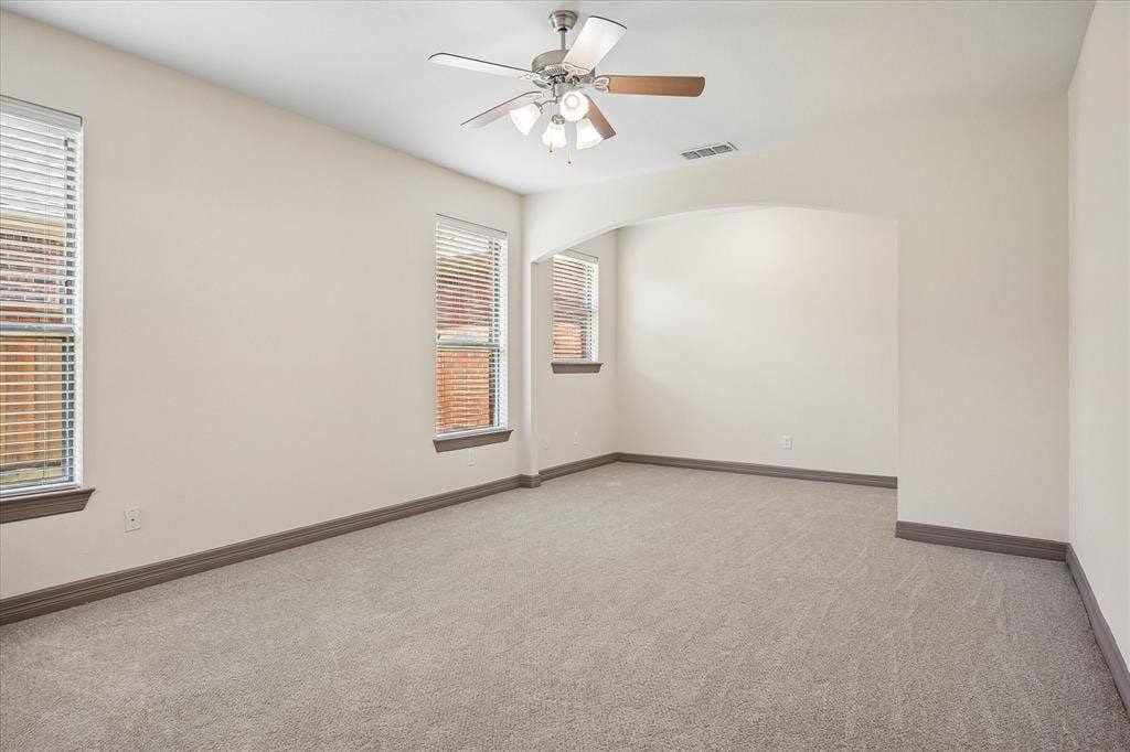 Carpeted room with a ceiling fan, multiple windows with blinds, and an arched doorway