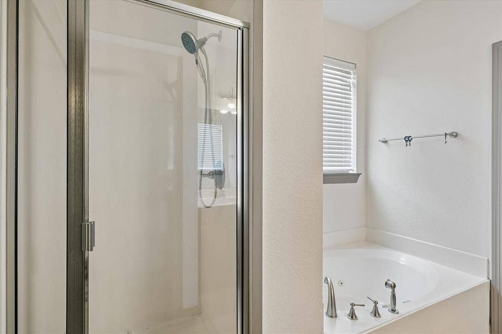 Glass-enclosed shower, corner soaking tub with deck-mounted brushed nickel fixtures, and a window with blinds