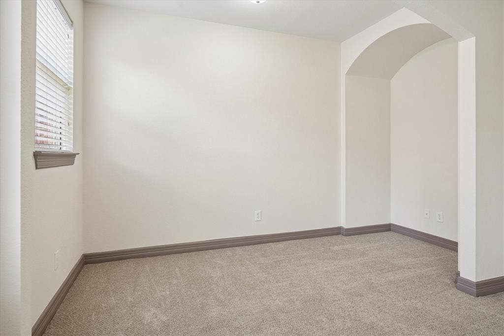 Arched entry, neutral carpeting, window with blinds, and white walls