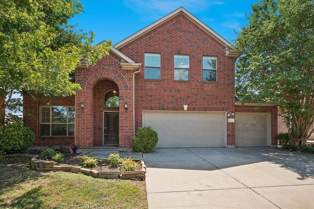 Brick exterior with a prominent arched entry, multiple windows, a two-car garage, an additional single-car garage, and landscaped planting beds